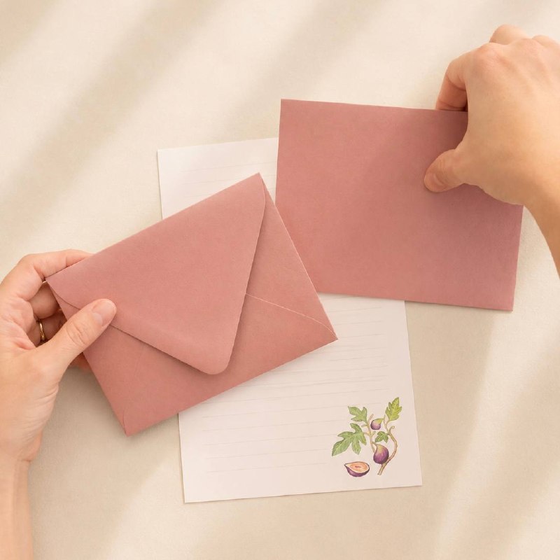 Hands holding a dusty-pink envelope above fig-patterned letter paper